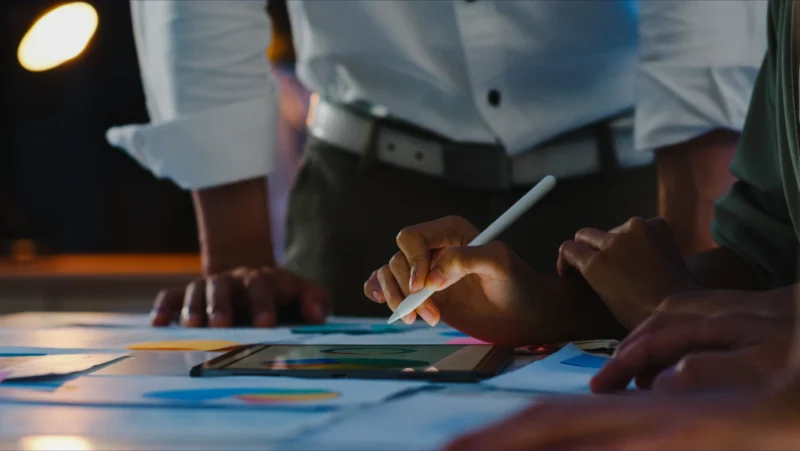Team al lavoro su un Proof of Concept: primo piano su una mano che utilizza uno stilo su un tablet, circondata da grafici colorati e documenti su un tavolo